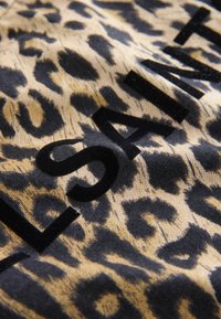 Khaaki ja jaal se bana leopard print kapra jo kaalay rang mein ek marhamati, velvety logo ke saath hai. Is design mein jaanwar ke naqsh aur zor daar likhai shamil hai.