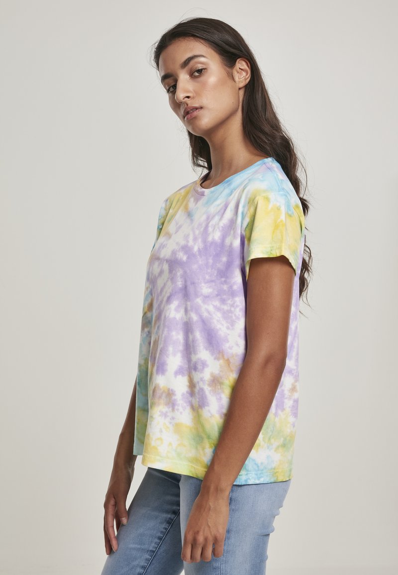 Bavlněné tričko s technikou tie-dye a uvolněným střihem. Hlavní barvy zahrnují fialovou, žlutou a modrou, s krátkými rukávy a kulatým výstřihem.