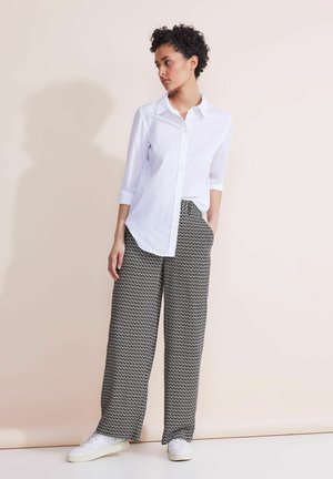 Camicia bianca a maniche lunghe abbinata a pantaloni larghi a fantasia bianca e nera e sneakers bianche.