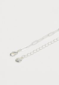 Silberne Kettenarmband mit flachen und runden Gliedern, einem Karabinerverschluss und einem Muschelanhänger. Polierte Oberfläche, leichtes Design.