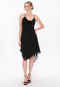 Fekete sifonruha spagetti pántokkal, vir�ágdíszítéssel a deréknál és aszimmetrikus szegéllyel. Simára kidolgozott textúra.