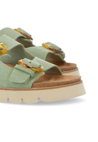 Green suede sandals with two wide straps, yellow circular accents, and a thick cream platform sole featuring scalloped edges.