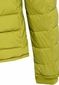 Manche et côté de veste matelassée verte en gros plan montrant les coutures matelassées et le bord-côte sur fond blanc.