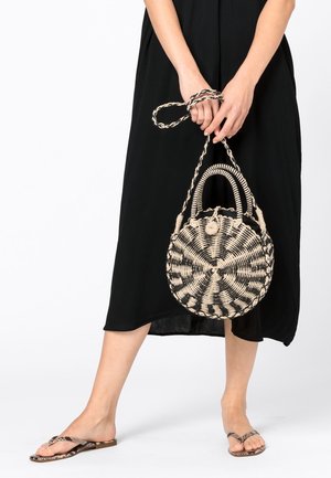Borsa tonda intrecciata in nero e beige con un motivo testurizzato, dotata di due manici e di una tracolla intrecciata. Indossata con un vestito nero.