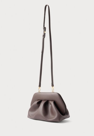 Καφέ δερμάτινο τσαντάκι χιαστί με μακριά ρυθμιζόμενη λουρίδα και μαλακό, μαζεμένο κάτω μέρος, τοποθετημένο σε ανοιχτό φόντο.