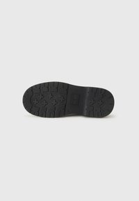 Semelle de chaussure noire avec un motif de semelle texturé, featuring étoiles et formes géométriques pour l'adhérence sur fond blanc uni.