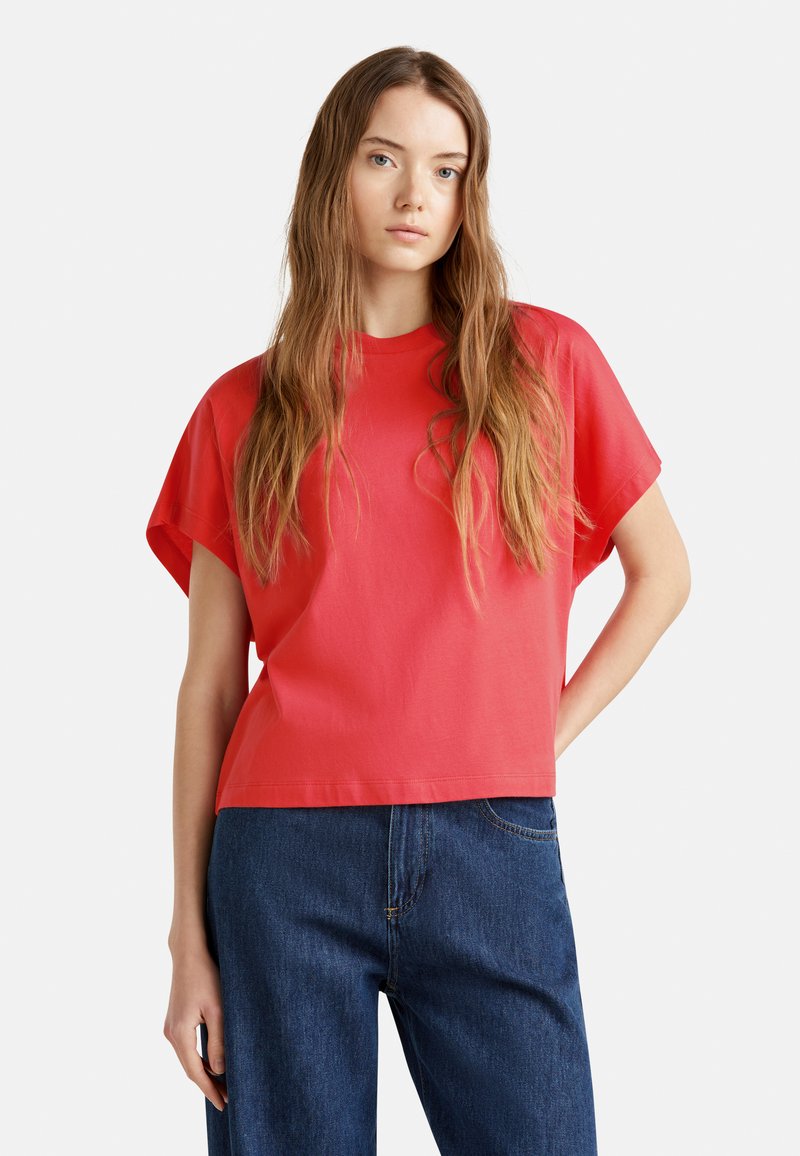 Rotes Kurzarm-T-Shirt mit rundem Halsauschnitt, lässiger Passform und glattem Stoff, kombiniert mit dunkelblauen Jeans.