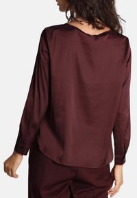 Blusa a maniche lunghe bordeaux in materiale morbido con vestibilità rilassata, scollatura rotonda e polsini con bottone. Vista posteriore, che mostra una drappeggiatura delicata.