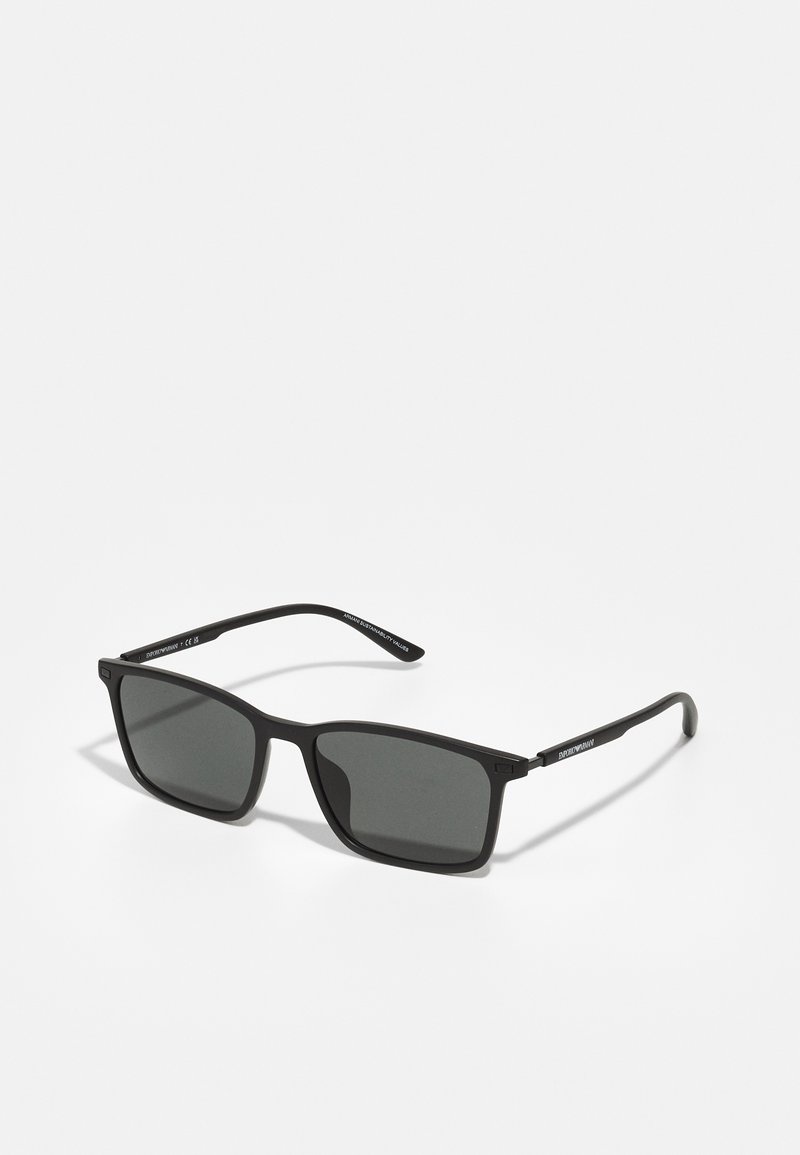 Ochelari de soare negri cu formă pătrată, cadru din plastic mat, lentile întunecate și brațe subțiri cu branding pe partea exterioară.