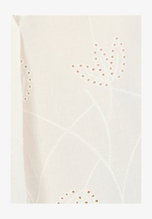 Tejido blanco delicado con patrones florales bordados y pequeños recortes circulares que forman elegantes diseños de flores.