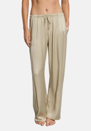 Beżowe spodnie z szerokimi nogawkami wykonane z satyny z pionowymi paskami, z elastycznym pasem, sznurkiem do wiązania, bocznymi kieszeniami, noszone na boso na jasnym tle.