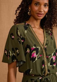 Zaļš kleita ar leopardu rakstu melnā, rozā un gaiši zaļā krāsā. Tam ir V-veida kakla izgriezums, uzbriedušas piedurknes un zelta maliņa ap kakla izgriezumu.