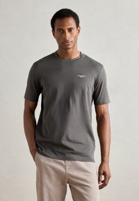 Herrkortärmad t-shirt i mörkgrå bomull. Rund hals med en liten vit logga på vänster bröst. Slät textur, figursydd design.