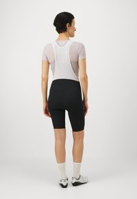 Schwarze Radsportshorts und ein enganliegendes, weißes Mesh-Trikot mit Racerback-Design, das strukturierter Stoff und minimalistische Akzente aufweist.
