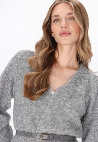 Grijze, gestructureerde trui met V-hals en lange mouwen, strakker getrokken in de taille met een grijze riem met een metalen gesp.