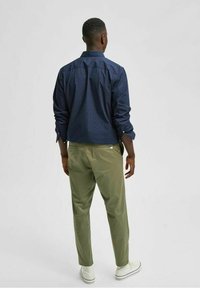 Navy blue button-up shirt with white polka dots, paired with light green trousers. Clean lines, fitted silhouette, and rolled sleeves.