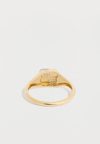 Arany gyűrű geometrikus mintával, sima peremmel és texturált négyzet alakú díszítéssel, amely kiemelkedő pontokat és áttetsző követ tartalmaz.