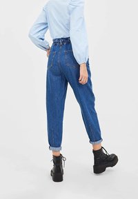High-waisted blue denim joggers with elastic waistband, rolled cuffs, and two back pockets, paired with black platform lace-up boots.