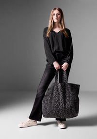Large black tote bag with a gray leopard print pattern, fabric material, sturdy handles, paired with a black blouse and jeans.