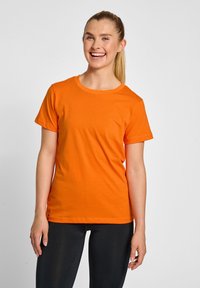 Oranje katoenen t-shirt met korte mouwen en een ronde hals, gecombineerd met zwarte legging, getoond op een glimlachend model.