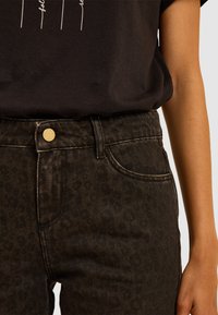 Jeans neri con un sottile motivo leopardato, caratterizzati da un bottone dorato, un classico design a cinque tasche e cuciture in contrasto.