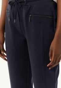 Marineblauwe broek met een gladde textuur, voorzakken met ritssluiting, een tailleband met trekkoord en een nauwsluitende pasvorm. Accentueert met zilverkleurige hardware.