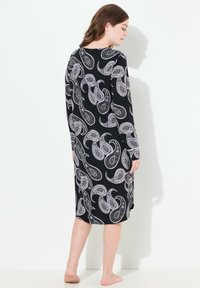 Mustapituinen pitkähiha dressi, jossa on valkoinen paisley-kuvio, polvipituinen, pehmeää kangasta, pyöreä pääntie ja lievät sivureiät.