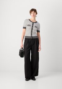Cardigan à rayures noires et blanches à manches courtes avec des boutons sur le devant, associé à un pantalon large noir taille haute et un petit sac noir.