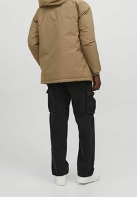 Tan vadderad jacka med huva, svarta cargobyxor med sidofickor, och vita sneakers. Enkel design utan synliga mönster eller detaljer.