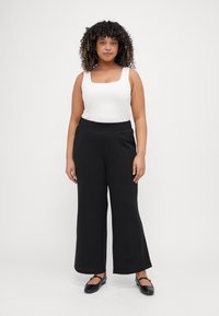 Black wide-leg trousers with a flat front, paired with a white, fitted tank top. The tank features a square neckline and thick straps.