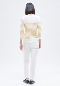 Wit met gele strepen lange mouwen top, gecombineerd met witte broek. Glad textuur, slim fit ontwerp en zwarte platte schoenen. Geen zichtbare hardware.