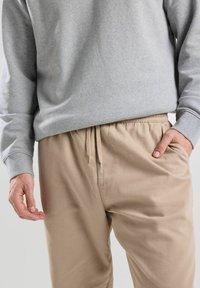 Sweat-shirt gris clair à manches longues associé à un pantalon beige à taille élastique et cordon de serrage. Tissu lisse et coupe décontractée ; sans motifs visibles.