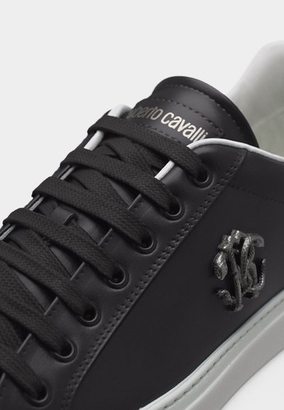 Baskets en cuir noir avec lacets noirs, semelle blanche, logo Roberto Cavalli sur la languette, et emblème métallique en forme de serpent sur le côté.