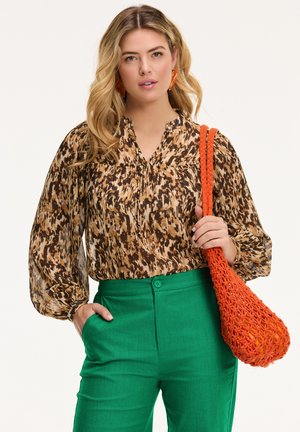 Brown and beige patterned blouse with puff sleeves, paired with green pants. Held is an orange woven bag with a textured design.