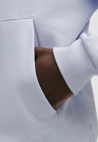 Lysblå sweatshirt med en lomme og ribbede manchetter. Stoffet har en blød struktur, og lommen er sømløst integreret i designet.