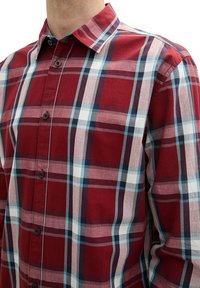 Red and blue plaid button-up shirt, featuring a collared neck, a pattern of varying size squares, and dark buttons along the front.