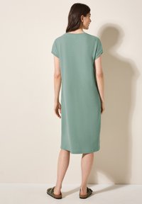 Zielona, bawełniana sukienka do kolan z krótkimi rękawami i luźnym krojem. Ma fakturowaną powierzchnię i opada prosto z ramion.