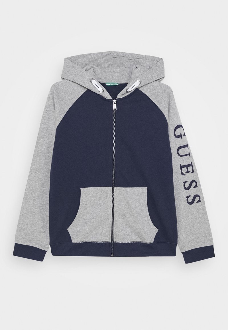 Sweat à capuche zippé pour enfant avec devant bleu marine et manches et capuche gris clair, avec le texte « GUESS » sur la manche droite et les poches avant.