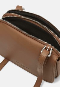 Borsa a tracolla in pelle marrone con più scomparti con zip, hardware argentato e una texture liscia. Cinghia regolabile attaccata.