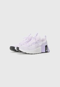 Baskets de sport lilas clair avec une tige texturée, semelle blanche plate, accents en caoutchouc noir, lacets à l'avant et une sangle à l'arrière.