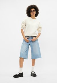 Krémová mikina, světle modré denimové culottes, černé platformové boty a bílé kotníkové ponožky. Mezi pozoruhodné detaily patří ohrnuté rukávy a roztrhaný lem.