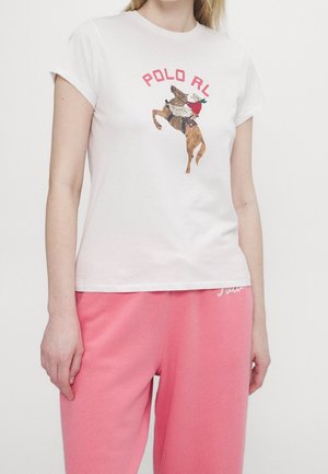 Vrouw draagt wit T-shirt met afbeelding van paard en ruiter en rode tekst "POLO RL", gecombineerd met losse roze broek.