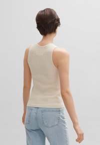 Beige geribbelde tanktop met een aansluitend ontwerp en ronde halslijn, gecombineerd met lichtblauwe high-waisted jeans, gezien vanuit de achterkant.