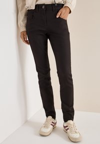 Zwarte denim jeans met een slim fit, met voorzakken en een knoopsluiting. Gecombineerd met crèmekleurige sneakers met bordeauxrode accenten.