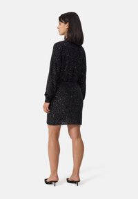 Minidress nero con paillettes, maniche lunghe, polsini a costine e silhouette aderente. Texture liscia con una finitura lucida in tutto il capo.