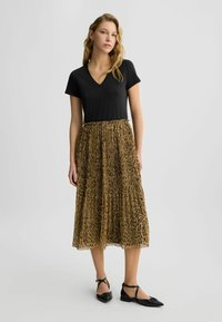Top nero a scollo a V abbinato a una gonna plissettata con stampa animale in toni terrosi. Scarpe nere piatte con un accento decorativo completano l'outfit.