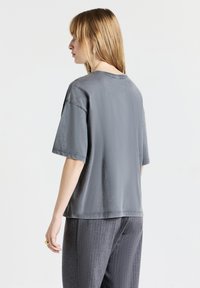 T-shirt en coton gris à coupe décontractée, à manches courtes et à encolure ronde, associé à un pantalon gris à rayures.