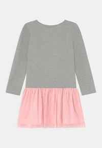 Dlouhý šedý šaty s růžovou tylovou sukní připevněnou v pase, rozložené na bílé pozadí.