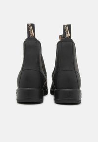 Bottines noires en cuir avec des panneaux élastiques sur les côtés et des languettes de tirage. Semelles robustes avec un motif de traction minimal, présentant des détails cousus le long des coutures.