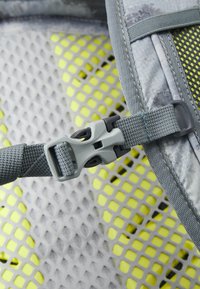 Correa ajustable gris con hebilla de plástico, que presenta un fondo de malla en gris y un patrón de cuadrícula en amarillo brillante. Se pueden ver detalles de tela con textura.